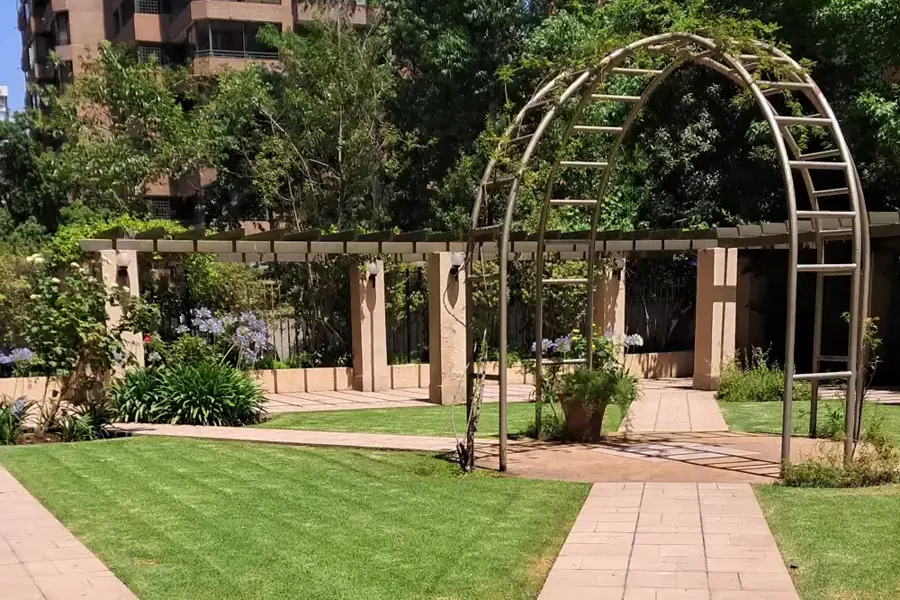 Pérgola metálica y senderos de baldosa en un jardín de condominio